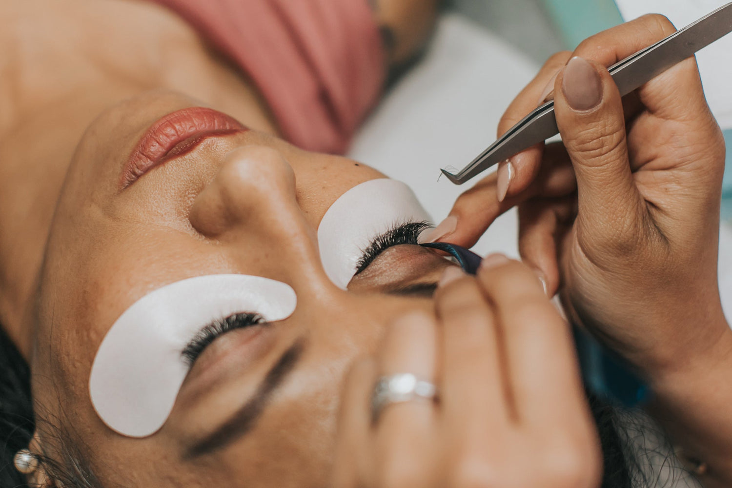 close-up of lash artist's hands holding a tweezer over the client's eyelash extensions